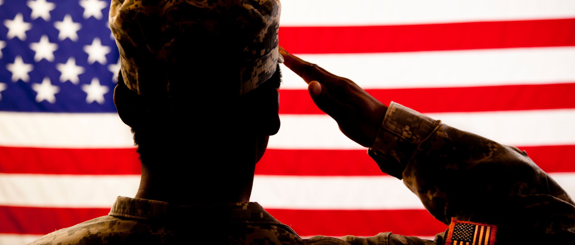 silhouette of man in military uniform saluting the US flag