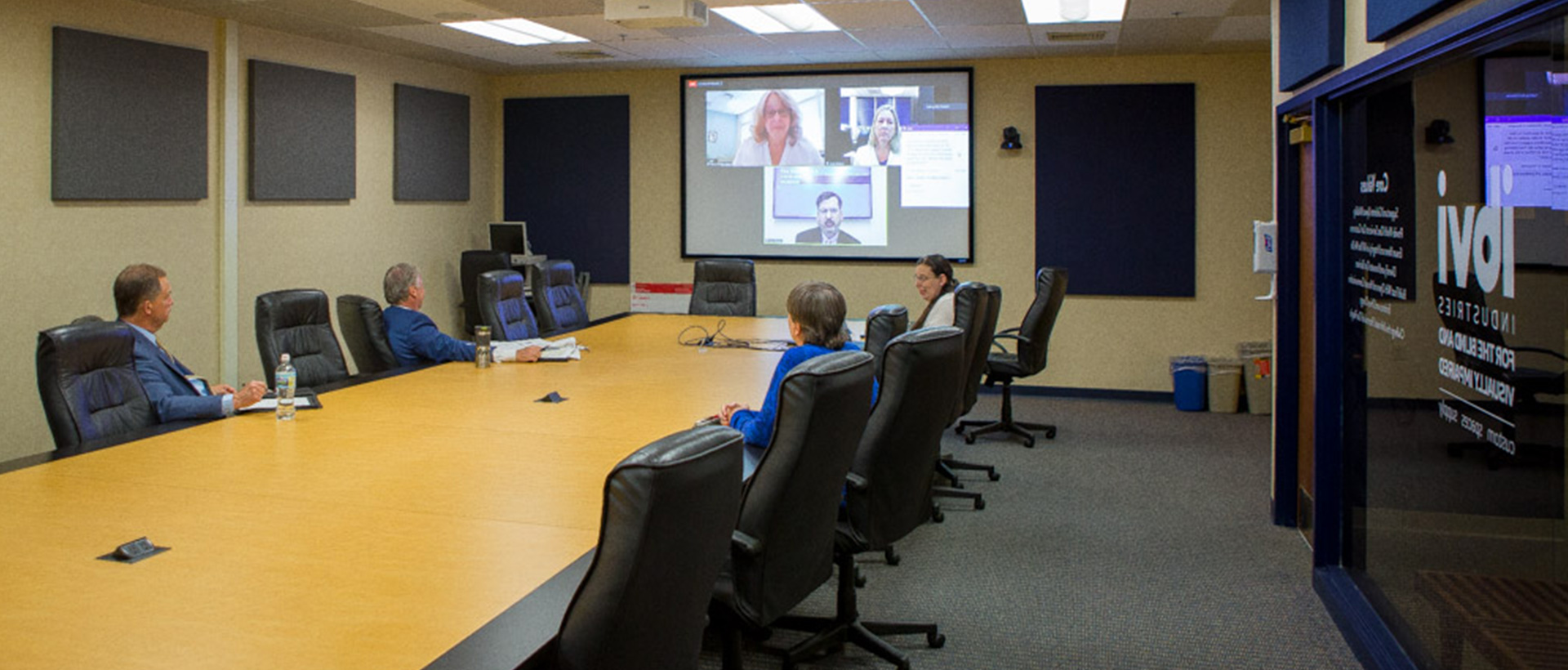 People sitting in a conference room video chatting with people on a projector screen