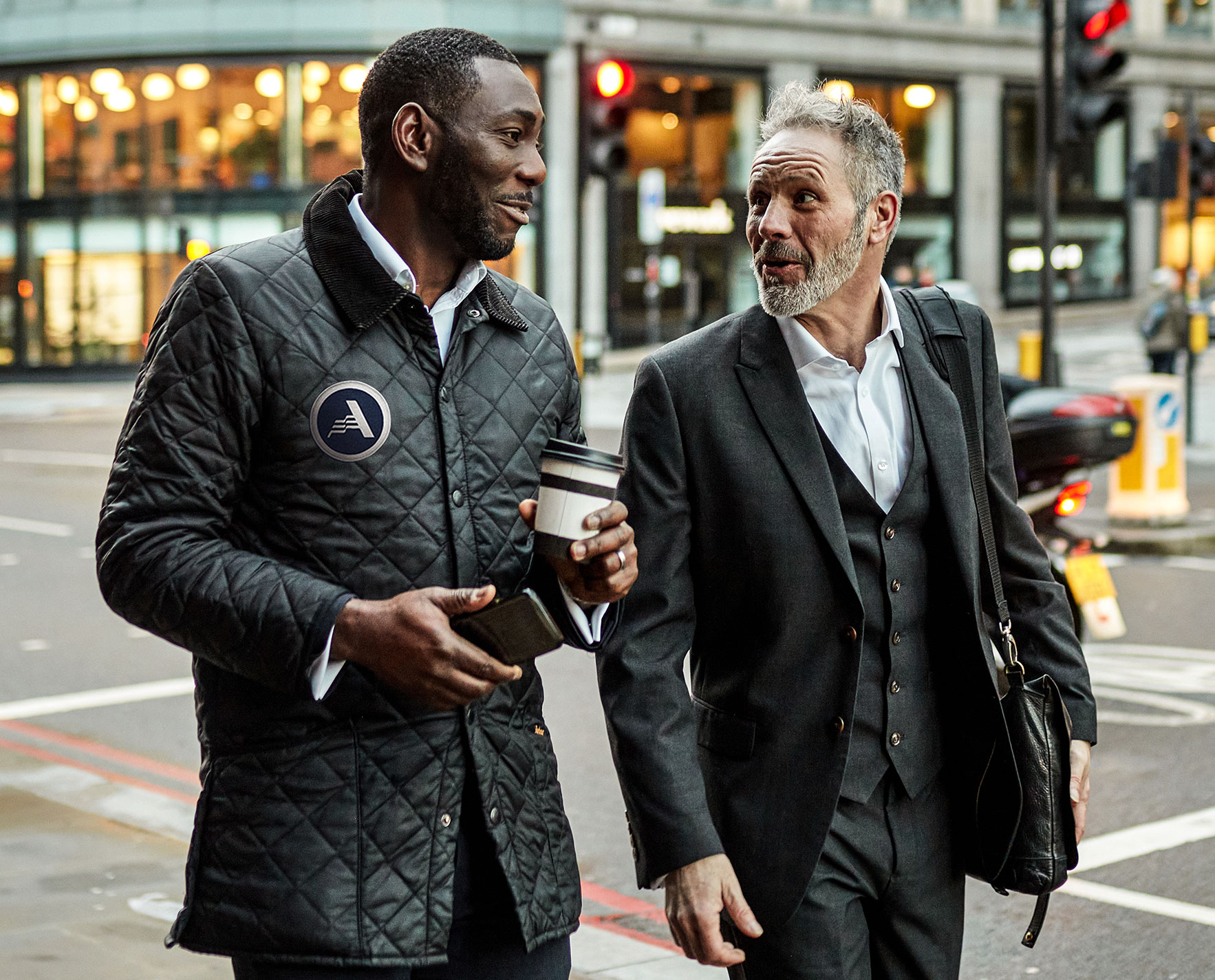 Two men walking across a city street talking to each other