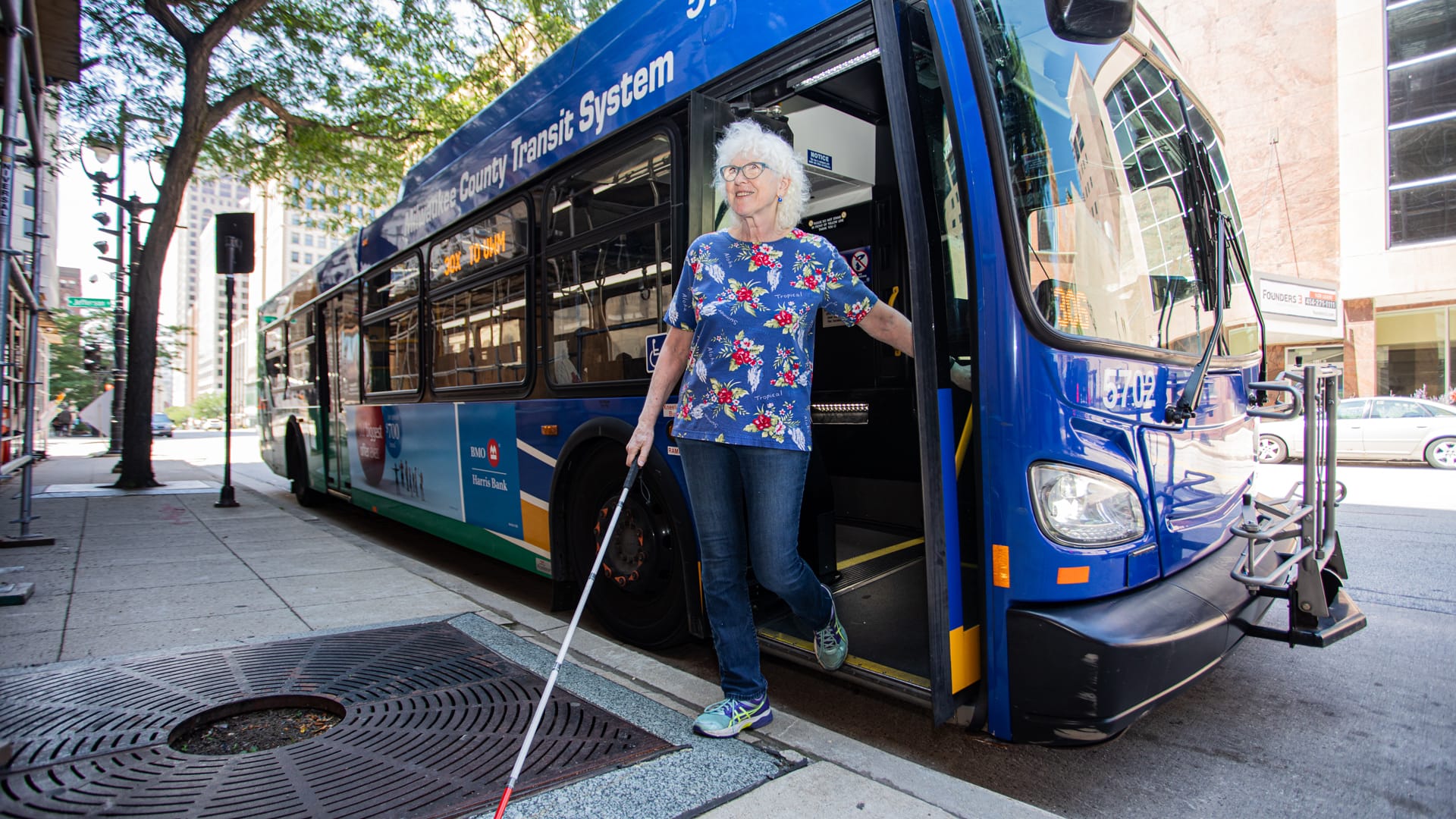 Woman using a white cane exiting a public bus.